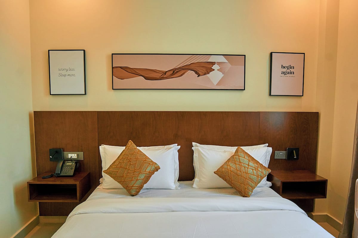 A hotel room with a large bed, two bedside tables, a telephone, and three framed pictures on the wall.