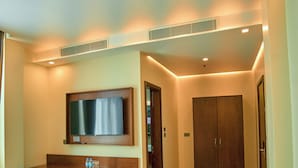 Ein Hotelzimmer mit einem Bett, einem Schreibtisch mit Computer, einem an der Wand montierten Fernseher, einem Kleiderschrank und einem kleinen Hocker.
