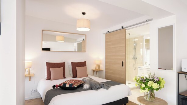 A modern bedroom with a large bed, bedside lamps, a mirror, and a small table with flowers.