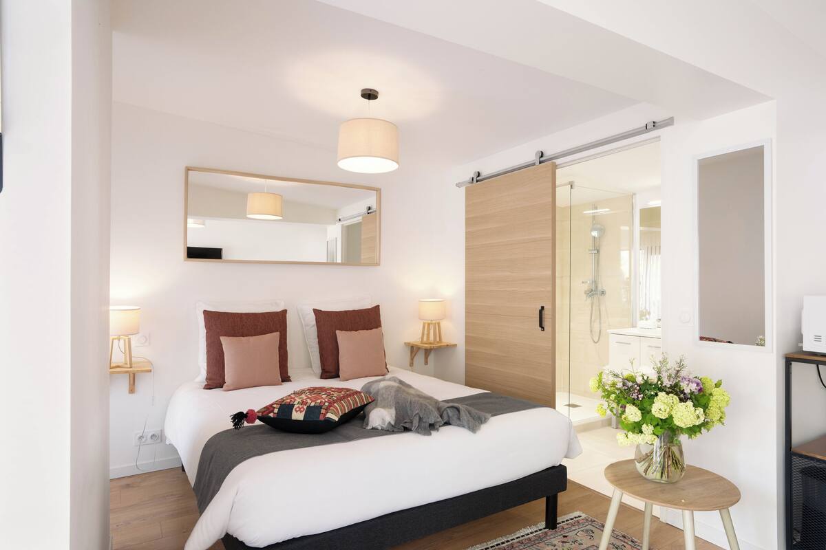 Un dormitorio moderno con una cama grande, lámparas de noche, un espejo y una pequeña mesa con flores.