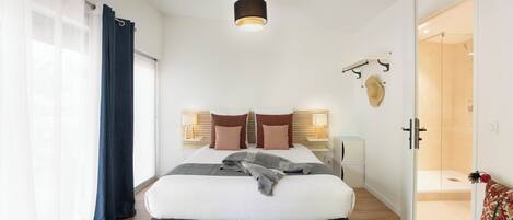 Un dormitorio moderno con una cama grande, una mesita de noche con lámpara, un armario y un baño visible a través de una puerta abierta.