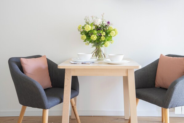 A dining table with two chairs, a vase of flowers, and white bowls and plates. - Les Studios de Honfleur (Honfleur)