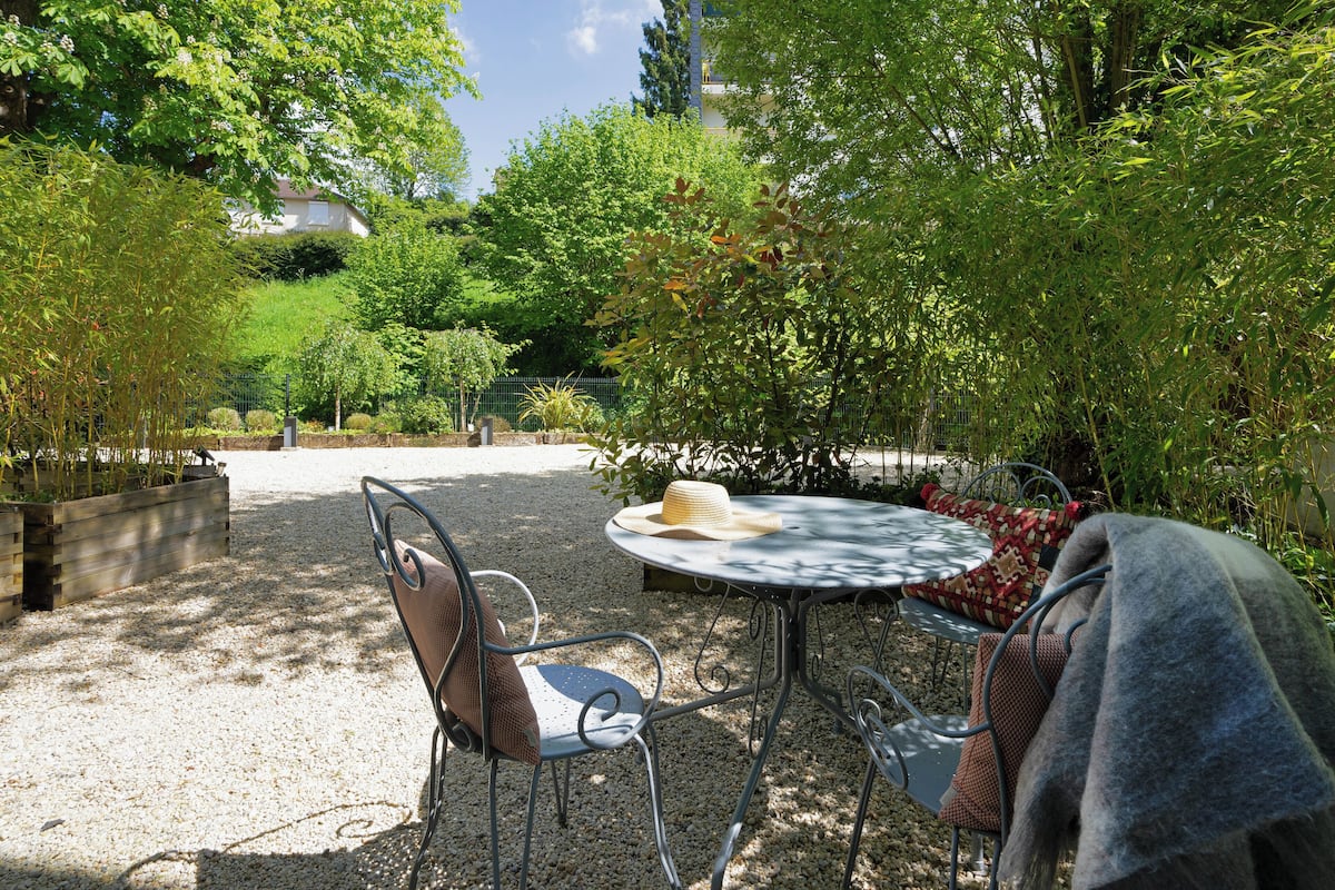 Un patio con una mesa redonda y dos sillas, rodeado de follaje y una cerca.