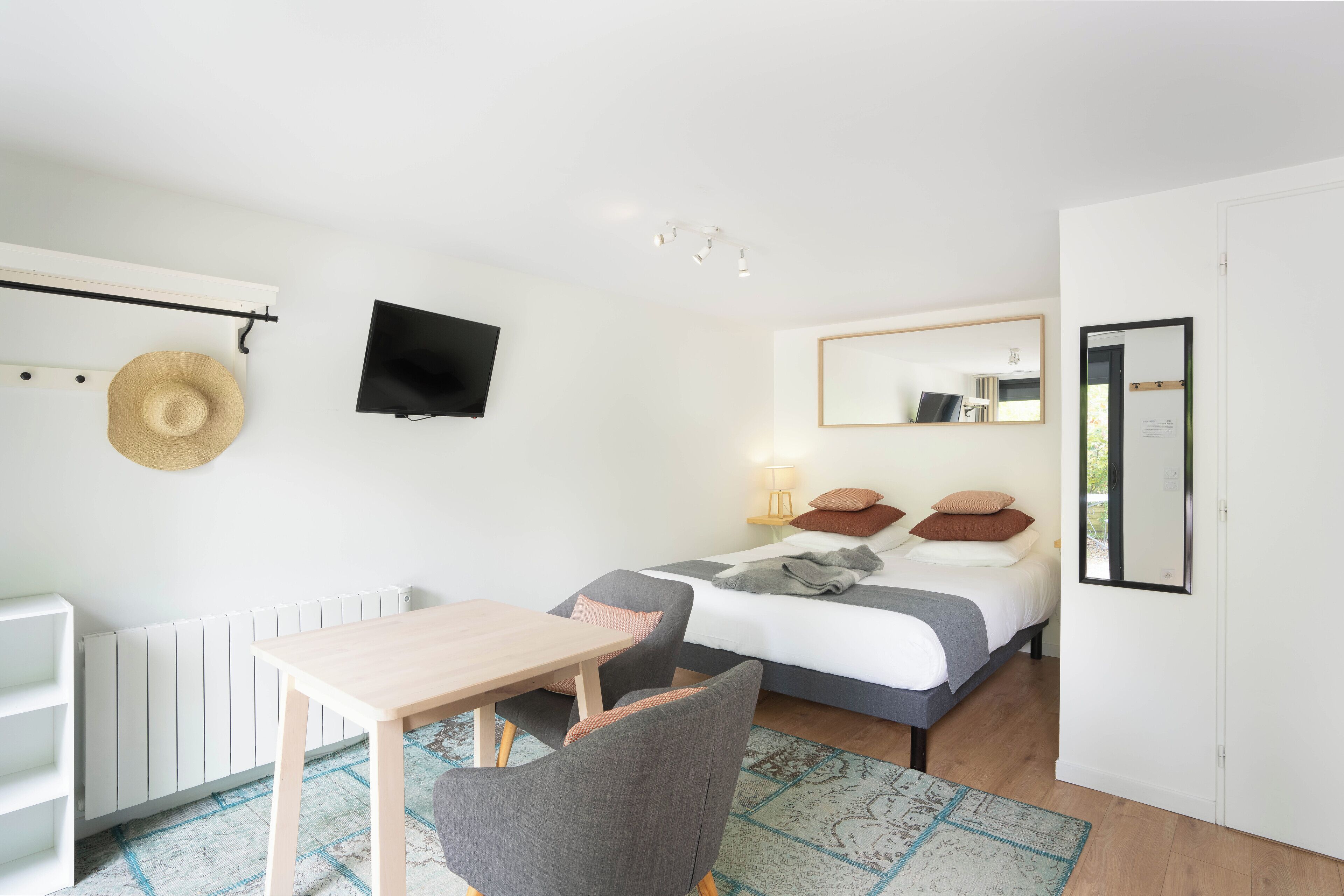 A bedroom with a bed, bedside table, chair, TV, and a radiator.
