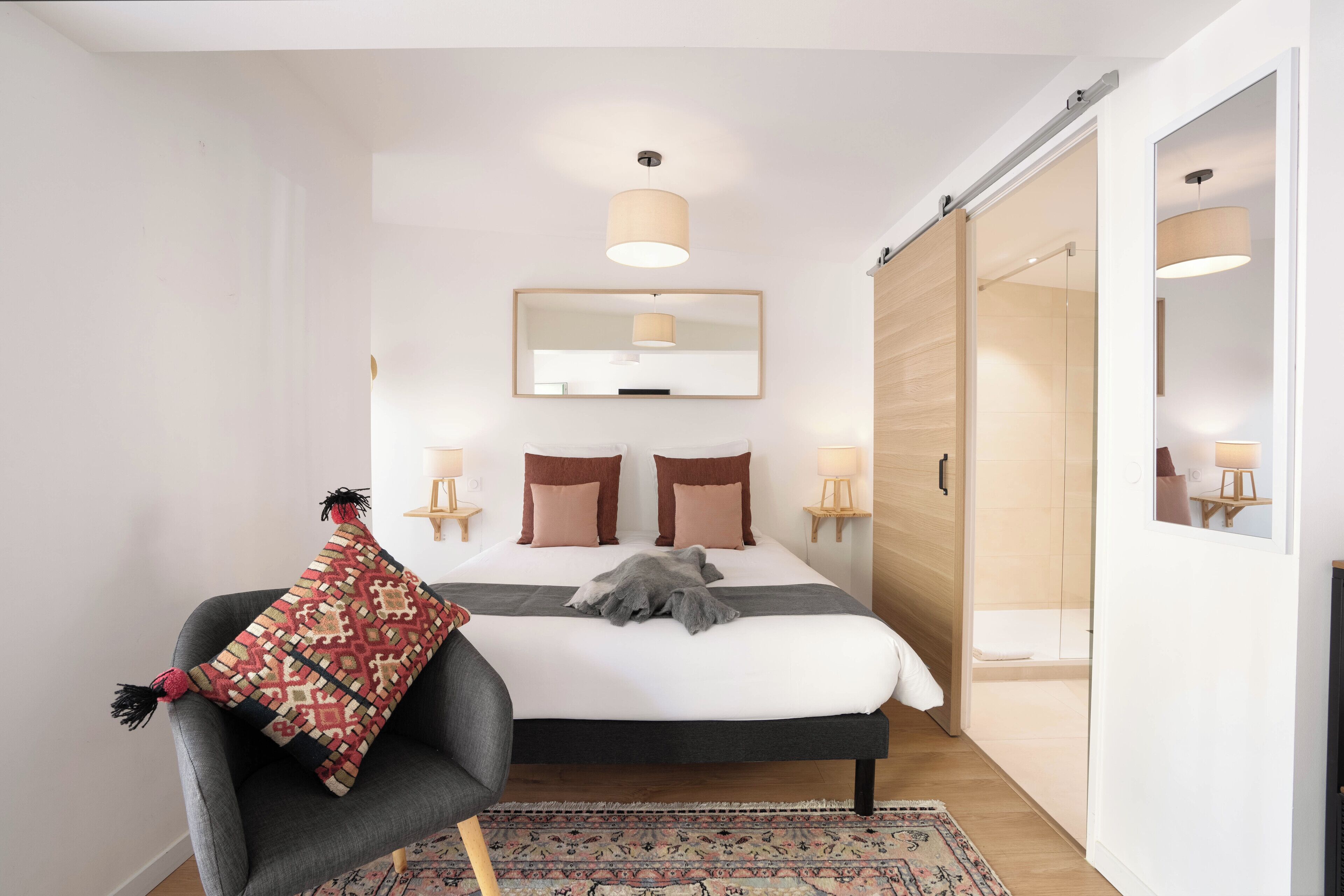 A modern bedroom with a large bed, bedside lamps, a mirror, and a sliding door leading to a bathroom.