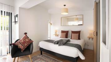 Un dormitorio moderno con una cama, un sillón con cojín estampado, un espejo grande y una lámpara colgante.