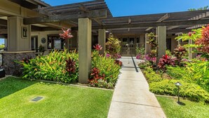 A hotel entrance with a covered walkway, stone pillars, and a variety of colorful plants. - Wailea Ekahi 37e 1 Bedroom Condo (Kihei)