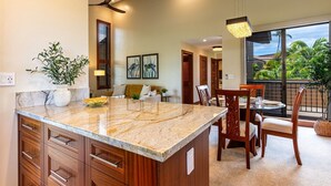 A kitchen with a marble island, wooden cabinets, and a dining area with chairs and a table. - Wailea Ekahi 37e 1 Bedroom Condo (Kihei)