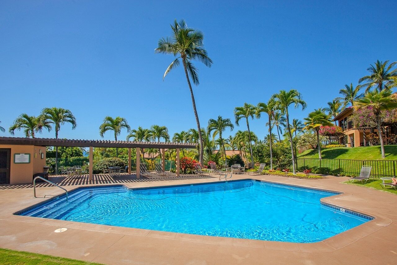 Ein Swimmingpool mit Pergola, Palmen und einem Gebäude mit einem Schild.