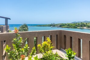Un balcon offrant une vue sur une mer calme, une jetée et une végétation luxuriante.
