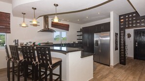 A modern kitchen with a central island, dark cabinetry, stainless steel appliances, and pendant lighting. - Pelican Penthouse -mangrove Dock 3 Bedroom Home by RedAwning (Roatan)