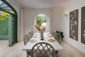 A dining area with a table set for six, a vase with dried pampas grass, and a window with curtains. - Sugar Hill - Jade Vine 4 Bedroom Villa (Holetown)