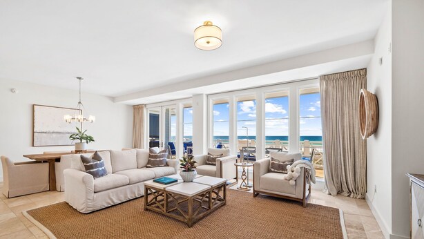 A spacious living room with a large window overlooking the sea, a cozy seating area with a sofa and armchairs, a coffee table, and a small side table. - Retreat Steps from Sugar-White Sand (Watersound)