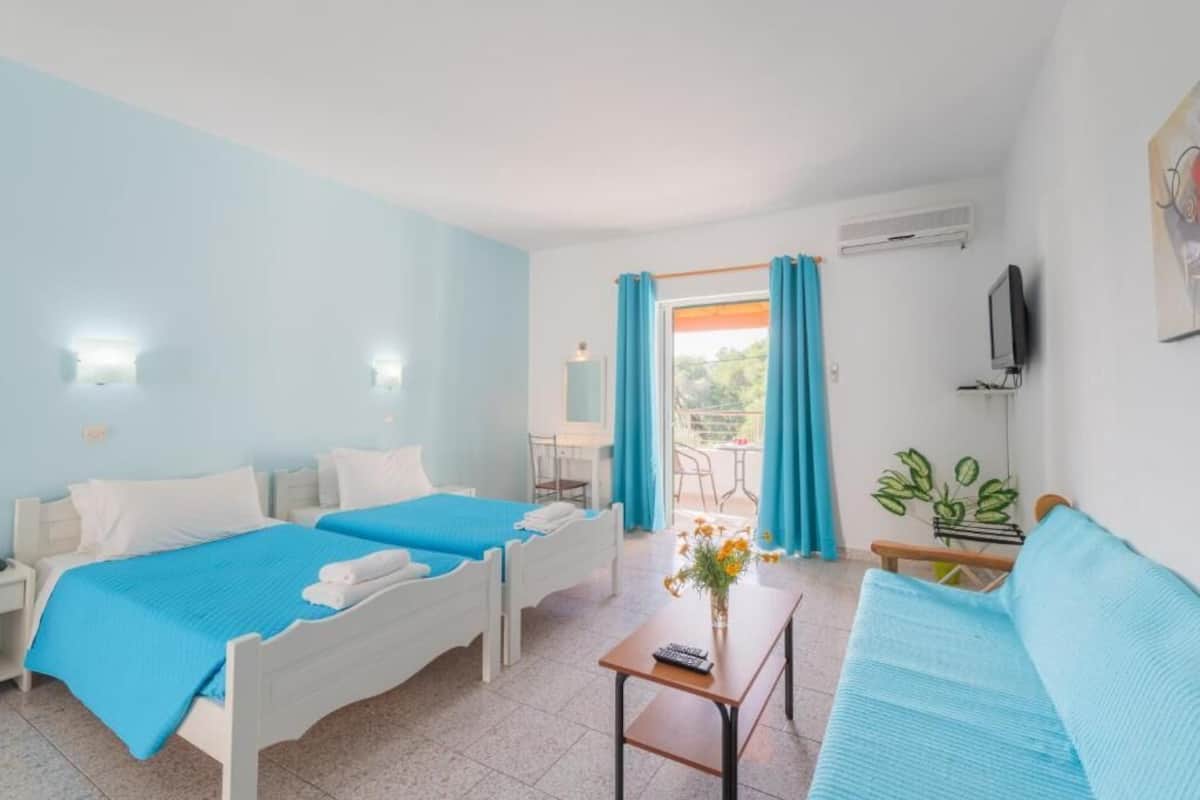 A hotel room with two beds, a sofa, a small table, a TV, and a balcony with curtains.