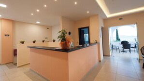 A reception area with a counter, potted plants, and a view of the outdoors. - Crystal Blue Hotel, Barbati (Corfu)