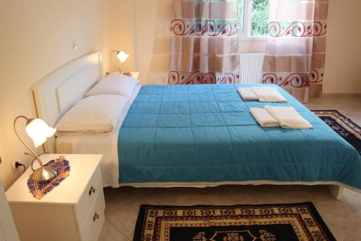 A neatly made bed with a blue bedspread and white pillows, a bedside lamp, and a patterned rug on the floor.