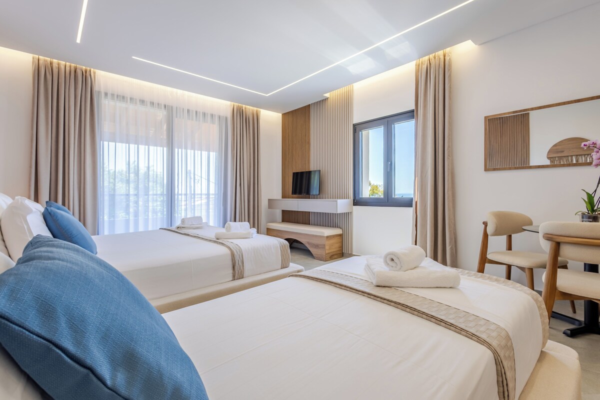 A hotel room with two beds, a desk, a TV, and a window.