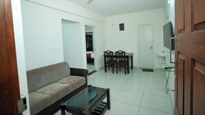 Una sala de estar con sofá, una mesa de centro, ventilador de techo, mesa de comedor con sillas y televisor.