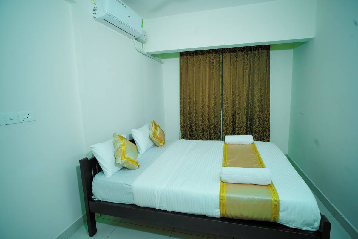 A neatly made bed with white and gold bedding, a dark wooden headboard, and a brown patterned curtain.