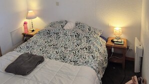 Un dormitorio con una cama, una mesita de noche, una lámpara, un cuadro de un ciervo y una mochila.