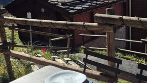 Mesa al aire libre con vista a la montaña, bancos de madera y un edificio rústico al fondo.