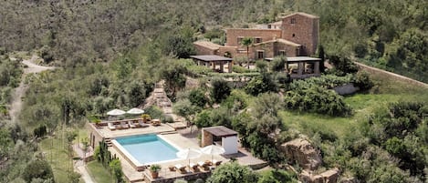 A large house with a swimming pool, surrounded by lush greenery and hills.