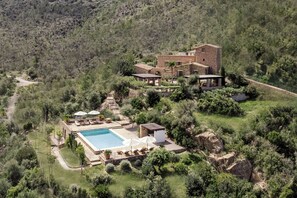 Une grande maison avec une piscine, entourée d’une végétation luxuriante et de collines.