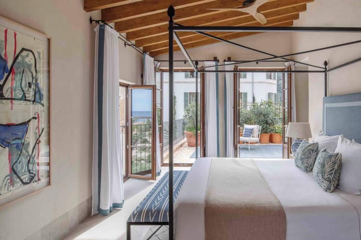 A bedroom with a four-poster bed, a large window, and a view of the outdoors.
