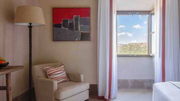 A hotel room with a bed, a chair, a table, a lamp, a painting, and a window with curtains.