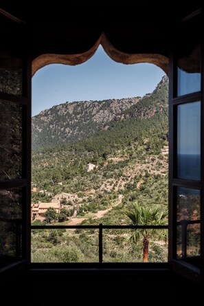 A view through an arched window of a mountainous landscape with scattered buildings and a palm tree. - Son Bunyola Hotel & Villas (Banyalbufar)