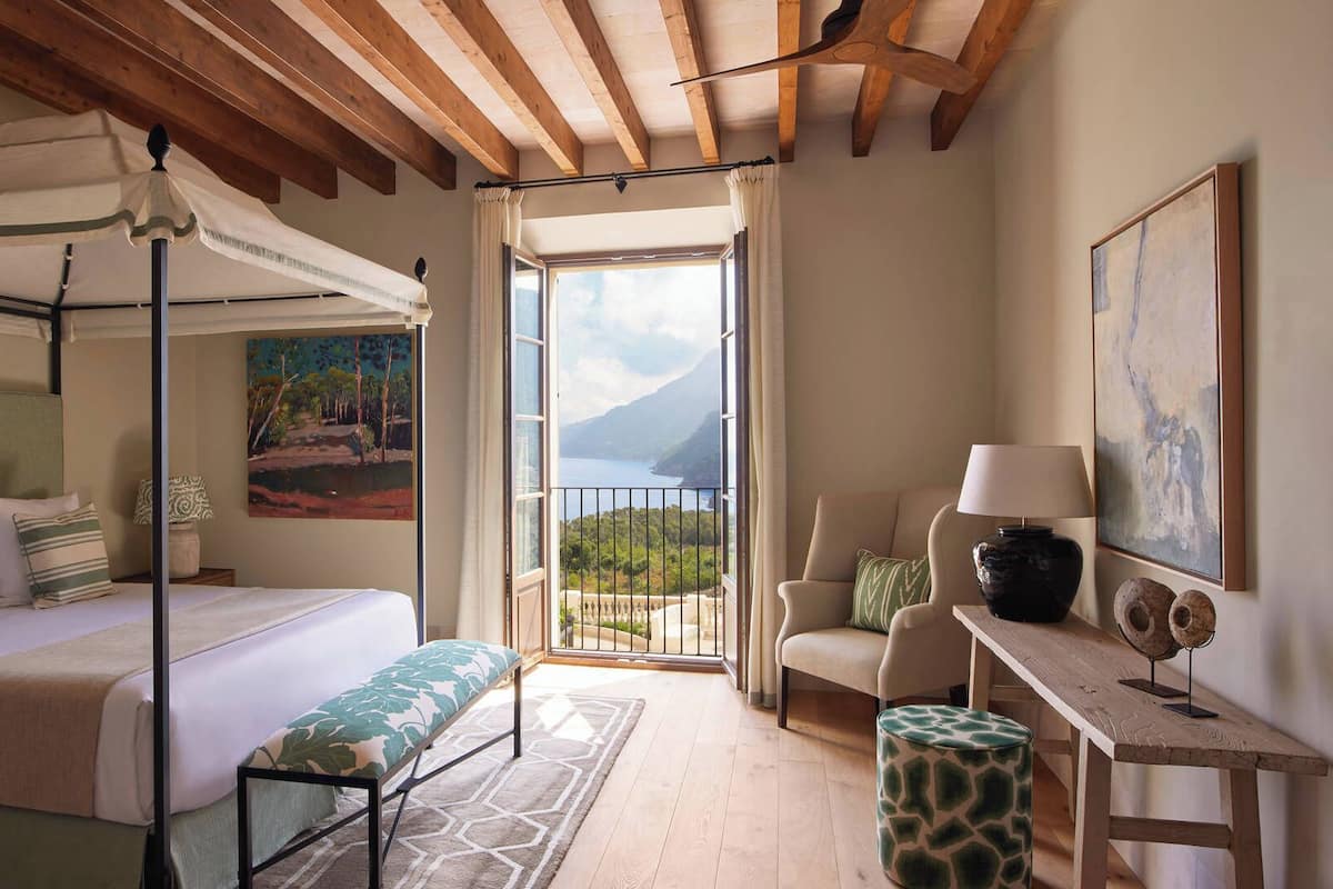 A bedroom with a bed, a bench, a chair, a table, and a painting.