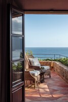 Un balcón con mobiliario de mimbre, una pared de piedra y vista al mar.