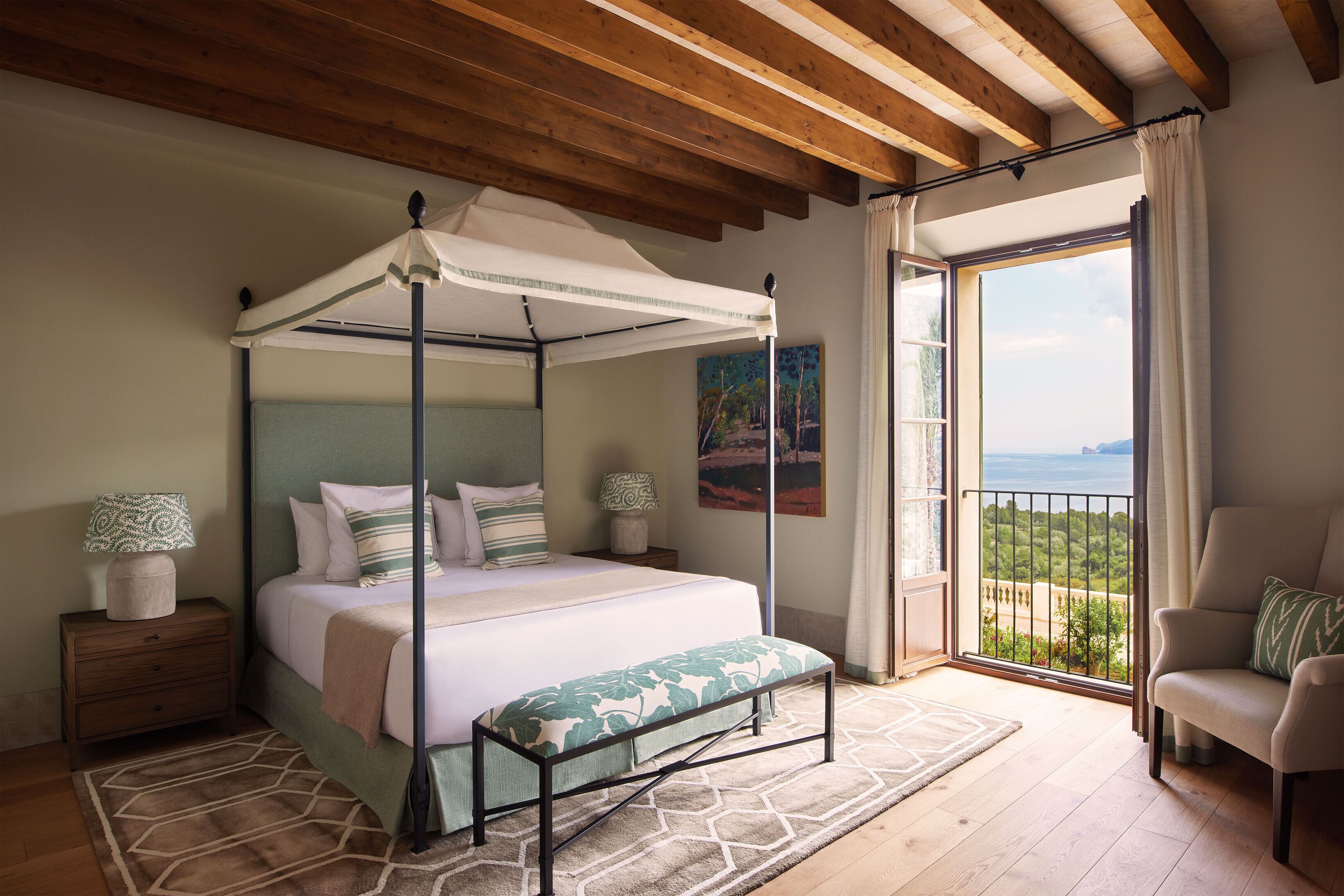 A bedroom with a four-poster bed, a balcony with a view, and a chair.