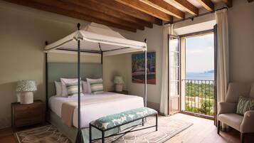 A bedroom with a four-poster bed, a balcony with a view, and a chair.