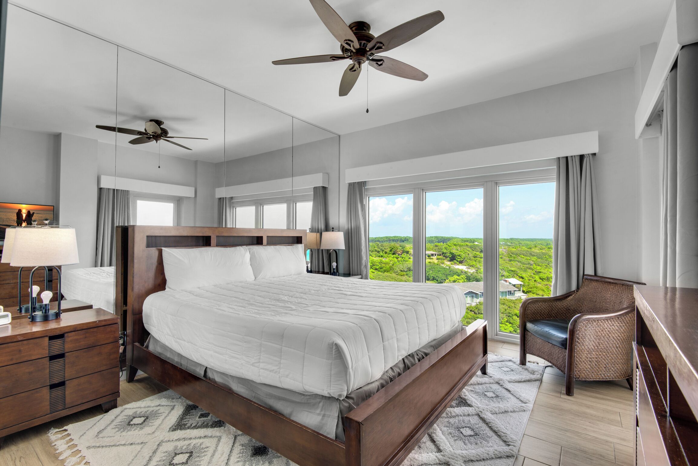A spacious bedroom with a large bed, two ceiling fans, a nightstand, a chair, and a view of the outdoors.