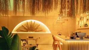 A modern bar area with a curved counter, wooden chairs, and a large plant. - Los Suites (Konyaalti)