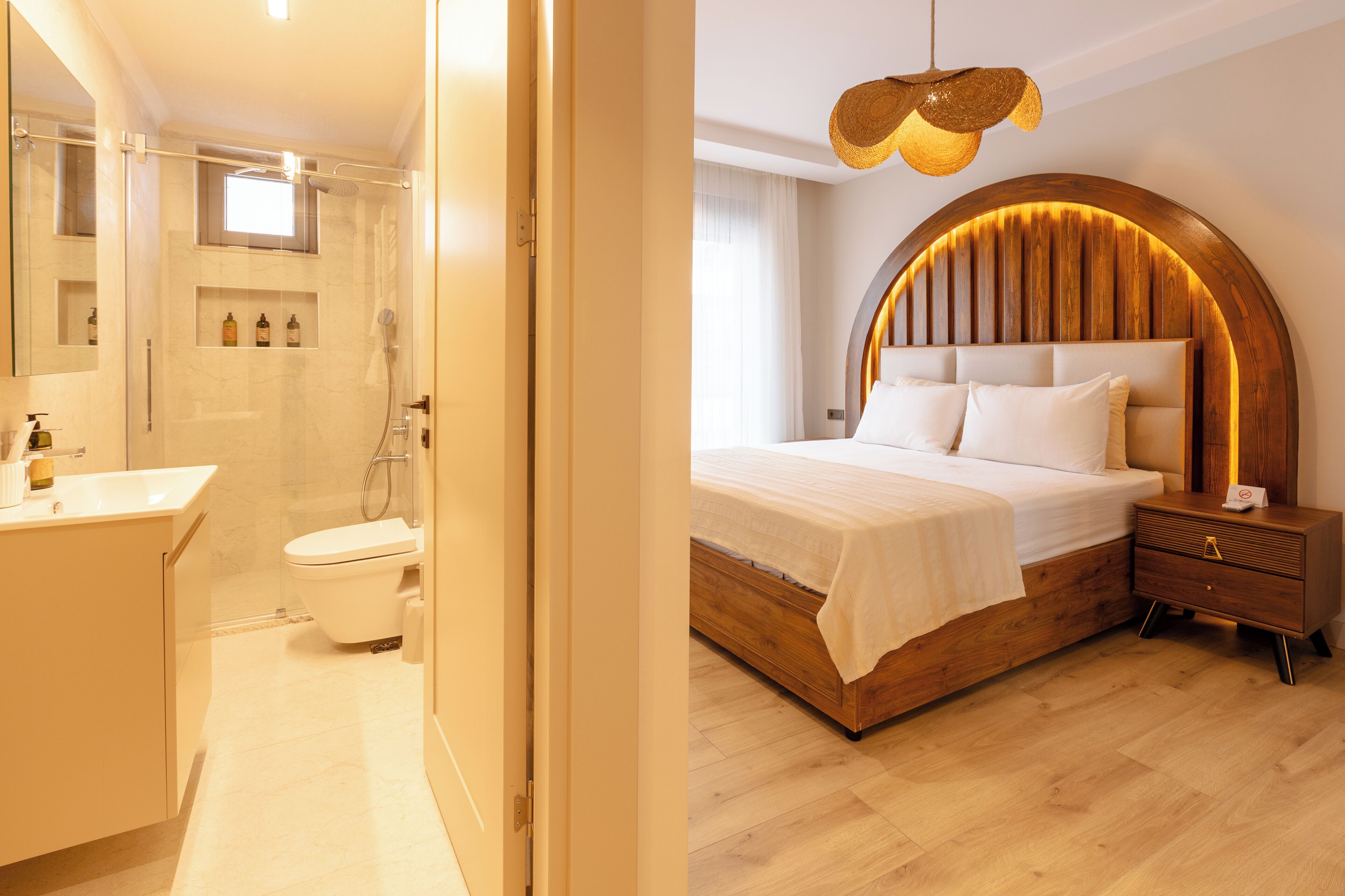 Un baño moderno con ducha, inodoro y lavabo. El dormitorio cuenta con una cama grande con cabecera de madera y una lámpara circular original.