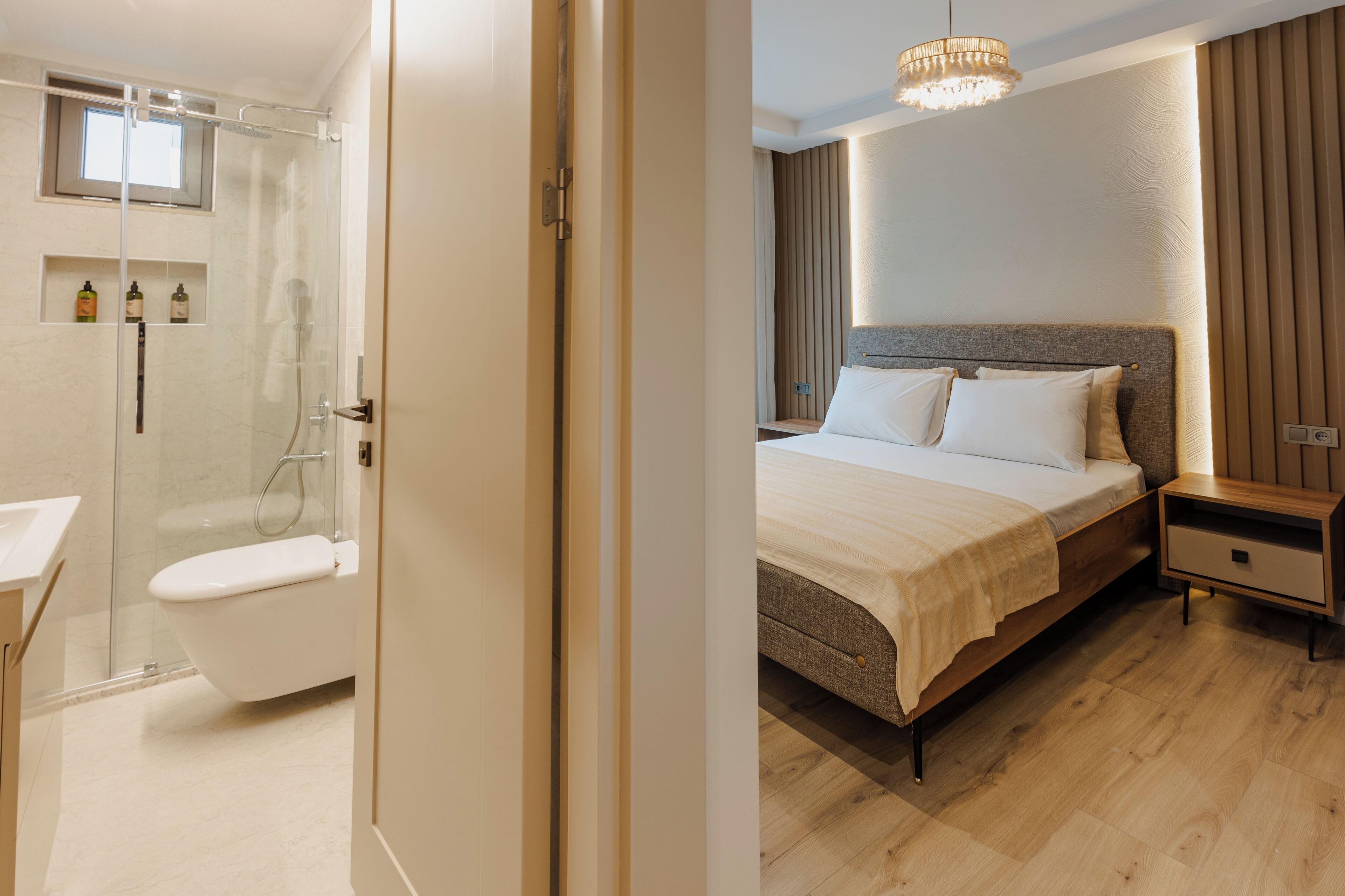 A modern hotel room with a glass-enclosed shower, a separate toilet, a wooden bed with a headboard, and a bedside table.