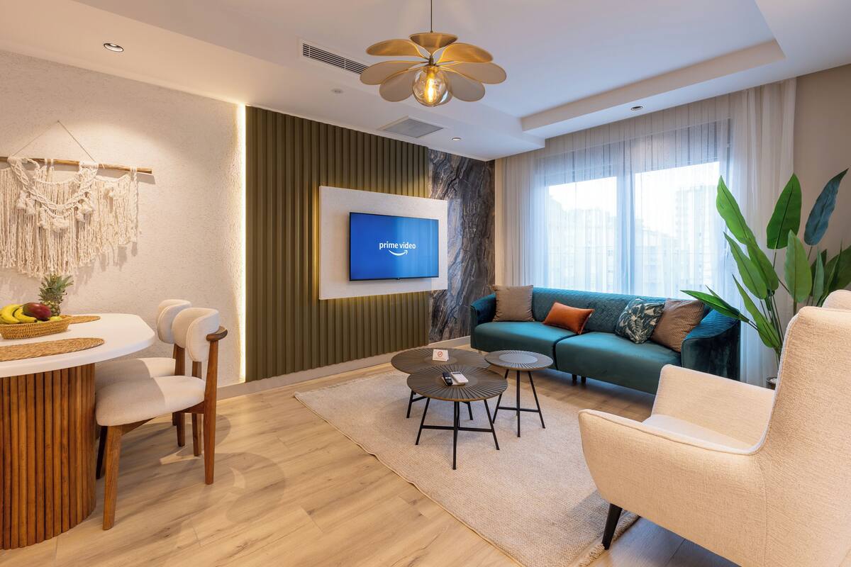 Uma sala de estar moderna com televisão de tela plana, mesa de centro redonda, sofá e um espaço de jantar com cadeiras e mesa de madeira.