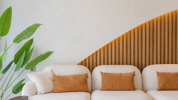 Een moderne woonkamer met een hoekbank, een grote groene plant en een wand van houten latten.