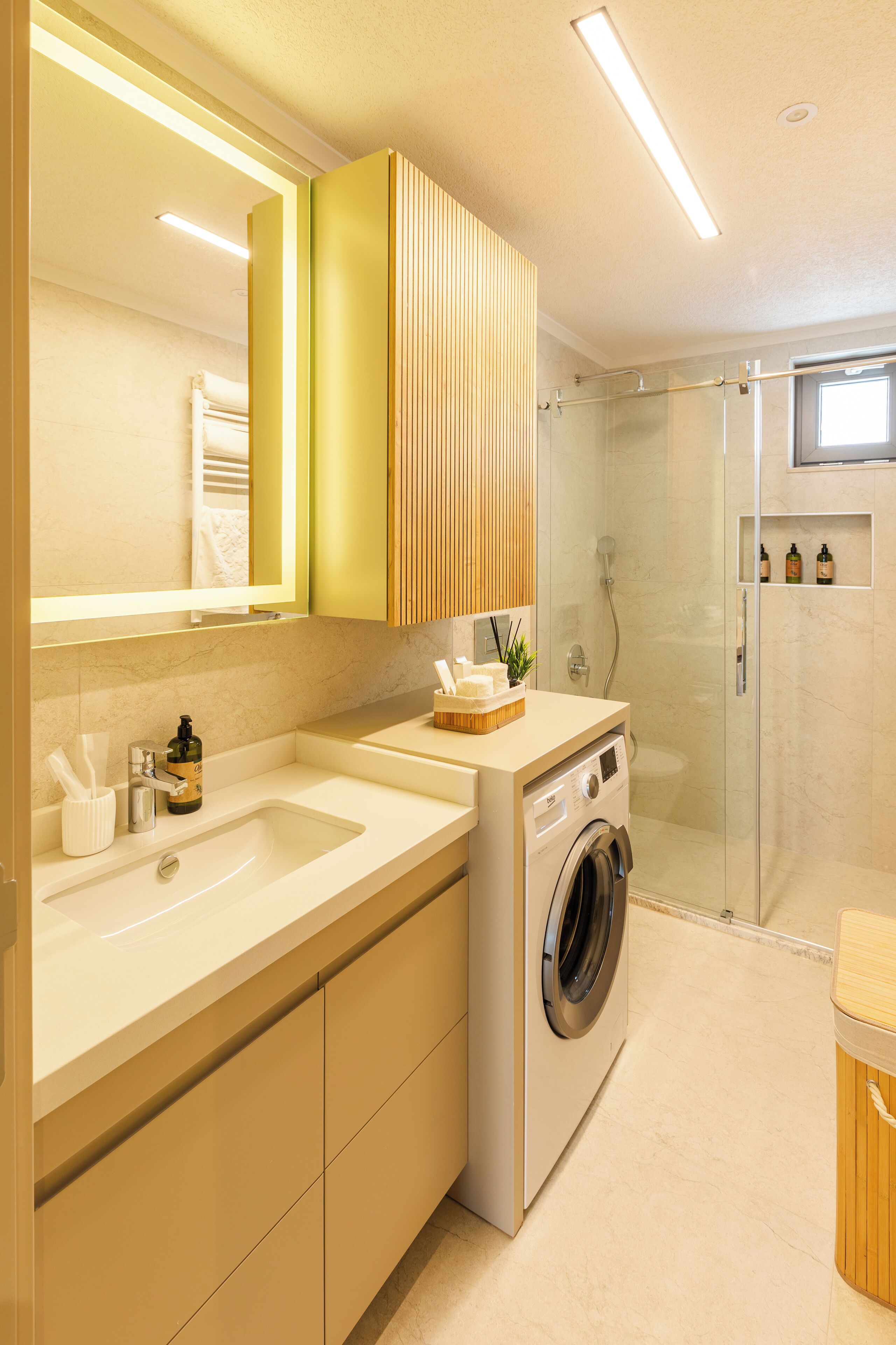 Une salle de bain moderne dotée d’un grand miroir, de deux vasques, d’un lave-linge encastré et d’une cabine de douche en verre.