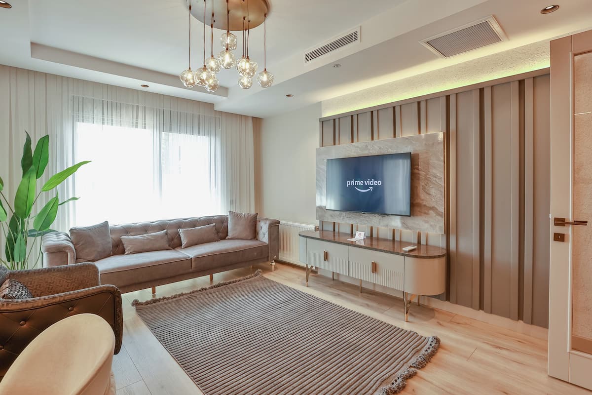 Uma sala de estar moderna com sofá, televisão na parede, planta grande e piso de madeira.