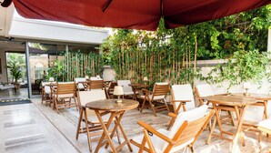 An outdoor patio area with wooden tables and chairs, surrounded by lush greenery and a red canopy. - Los Suites (Konyaalti)