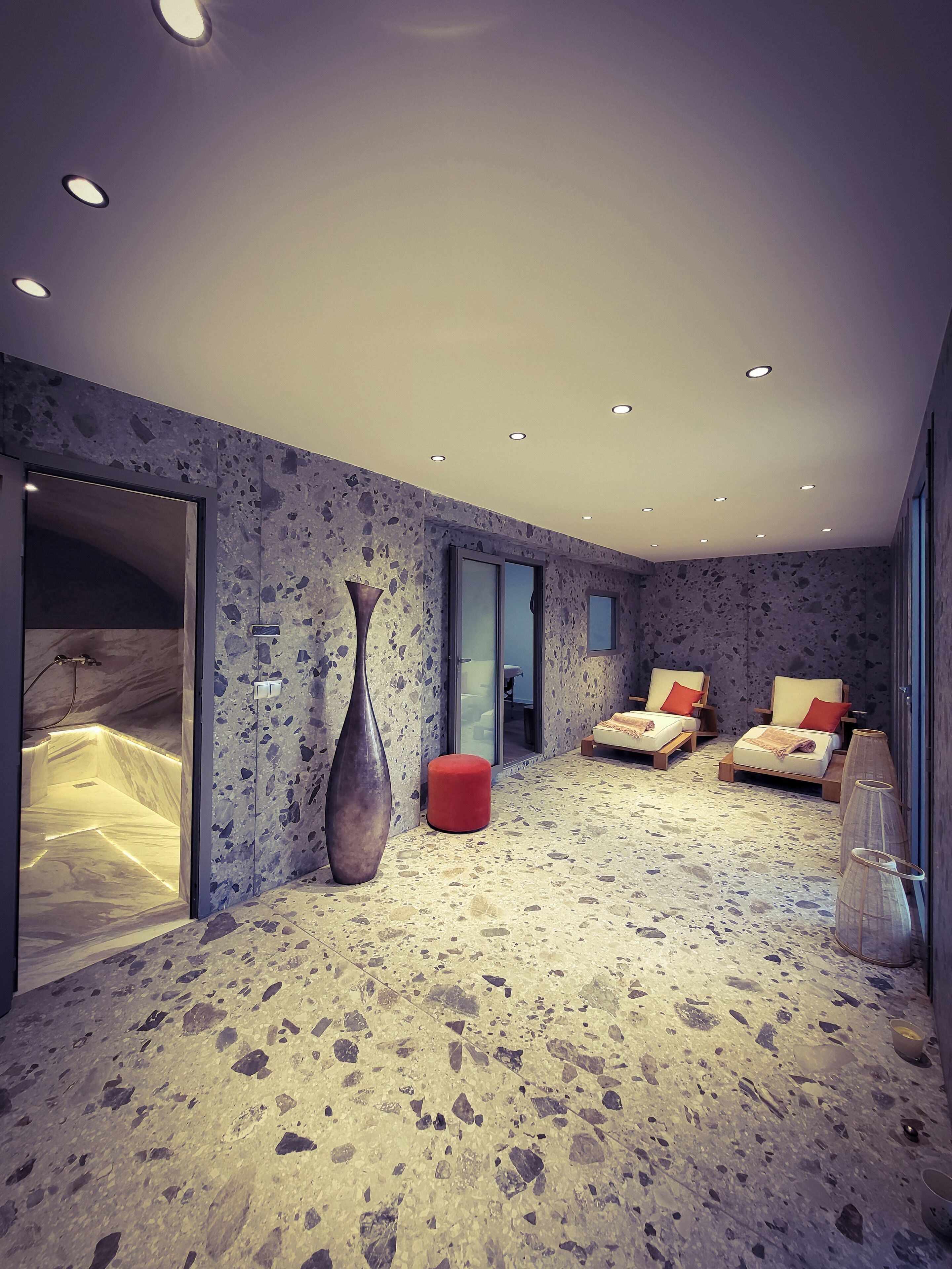 A modern bedroom with a large window, a bathtub, and two beds with red pillows.
