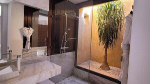 Un baño moderno con un espejo grande, un lavamanos de mármol y una zona de ducha con mampara de vidrio y una planta en maceta.