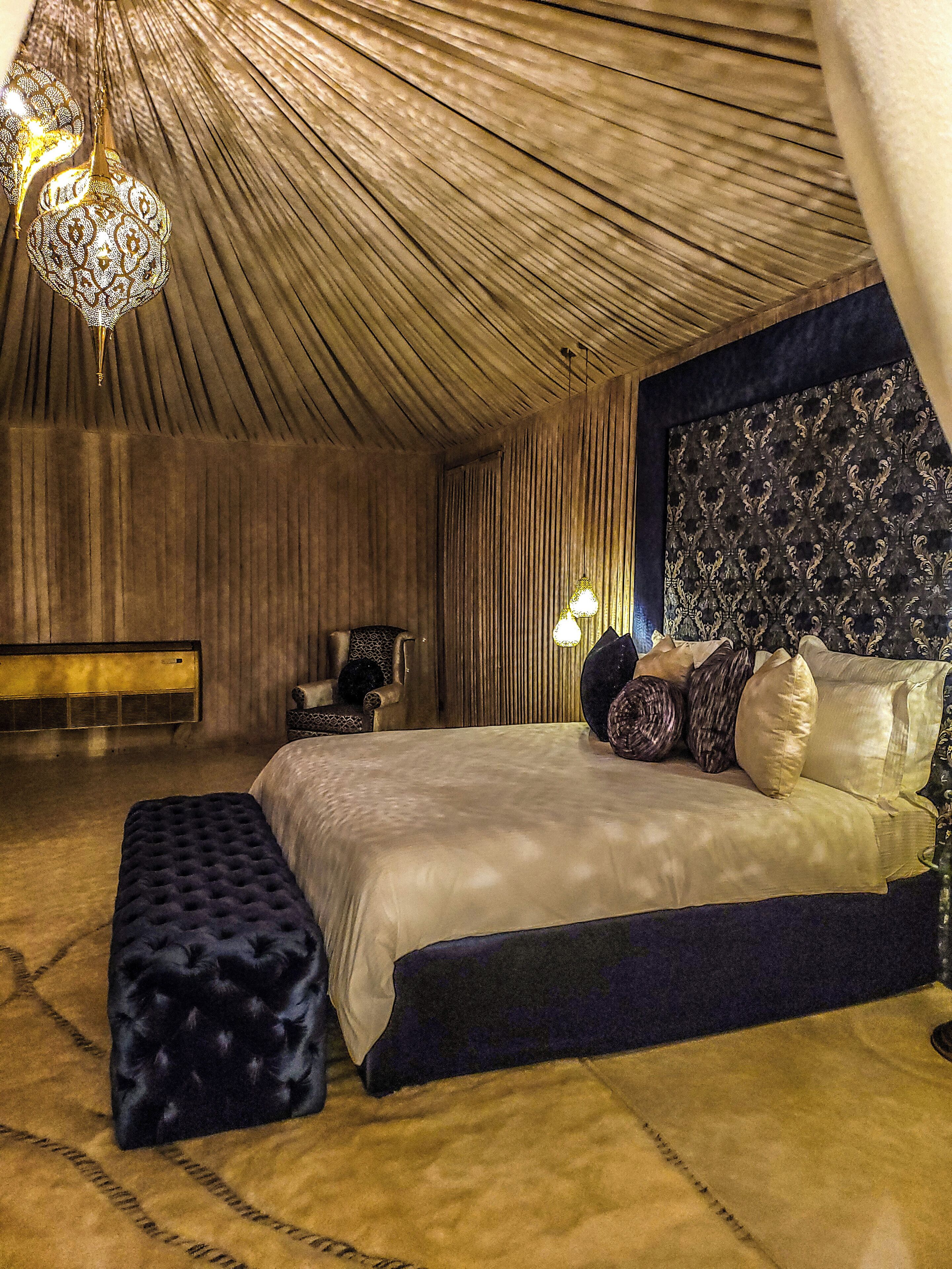 A bedroom with a large bed, a bench, a chair, and a patterned wall.