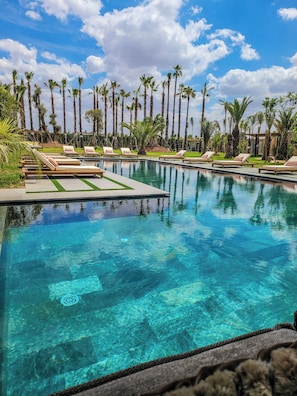 A clear pool with lounge chairs and palm trees in the background. - Villa Oxygène Marrakech Suites & Spa  (Marrakech)