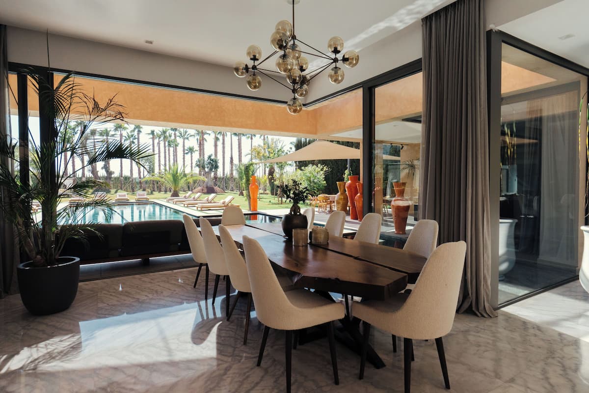 A modern dining area with a large table, multiple chairs, and a view of a pool and garden.