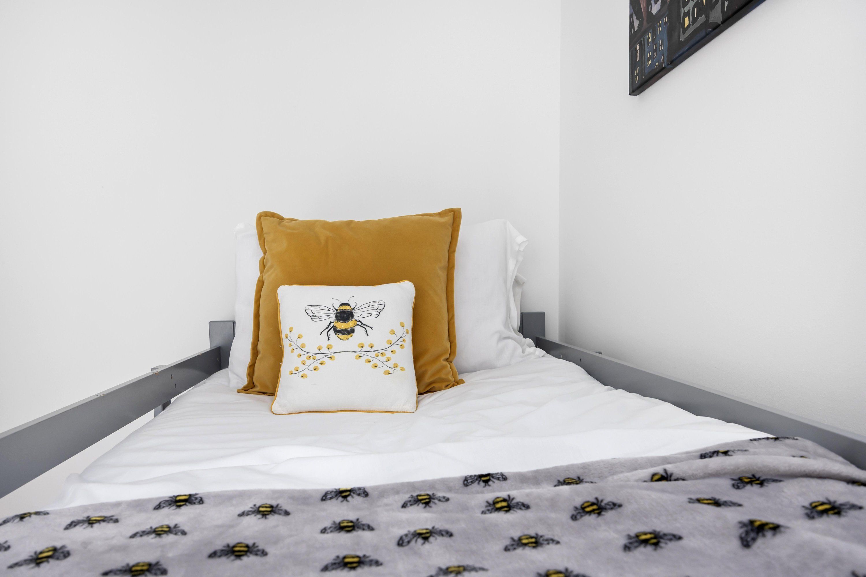 Un letto con materasso bianco, un cuscino color senape e un cuscino bianco con un disegno d'ape.