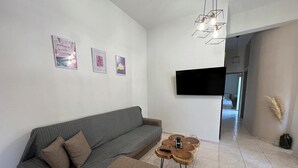 Una sala de estar moderna con un sofá gris, un otoman marrón, una mesa de centro con patas de madera y un televisor de pantalla plana montado en la pared.